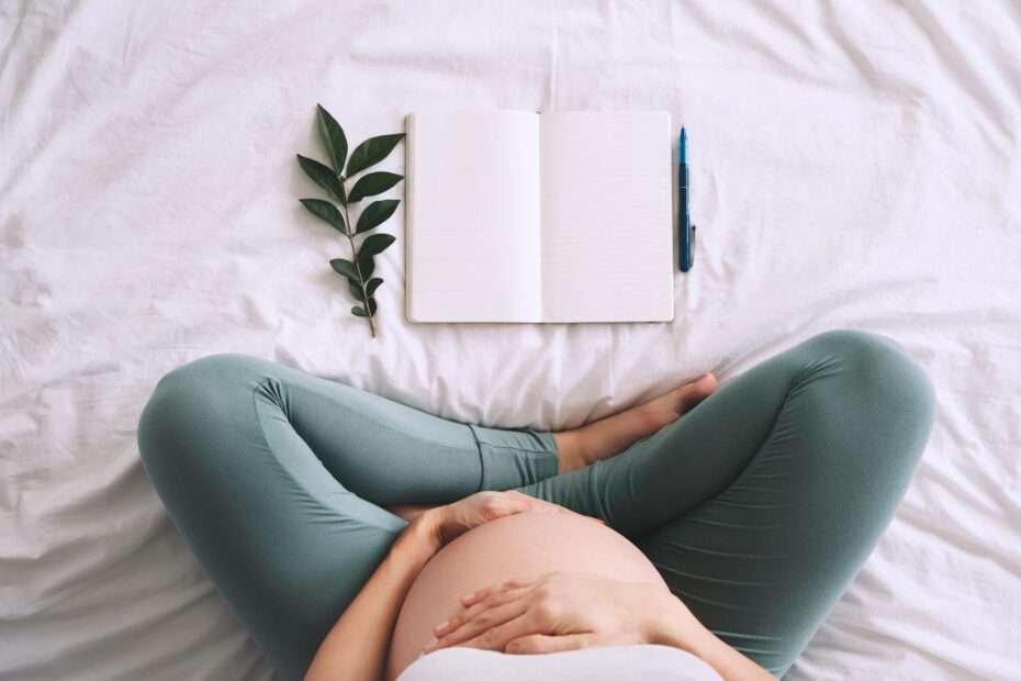 Schwangere Frau sitzt im Bett und schreibt Tagebuch. 